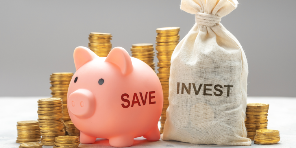 Piggy bank labeled “save” next to a money bag labeled “invest” with stacks of coins in the background 