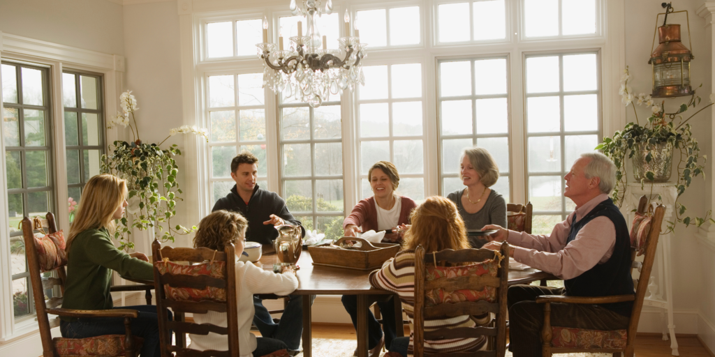 A multigenerational family gathered around a dining room table sharing conversation in a bright, sunlit home, representing the importance of family communication and legacy planning.